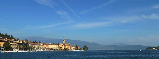 Trip Urlaubsreif beliebte Urlaubsziele am Gardasee -  Mit einer Fläche von 370 km² ist der Gardasee der größte See Italiens. Es liegt am Fuße der Alpen und erstreckt sich über drei Staaten: Lombardei, Venetien und Trentino. Die maximale Tiefe des Sees beträgt 346 m, er hat eine längliche Form und sein nördliches Ende ist sehr schmal. Dort ist der See von den Bergen der Gruppo di Baldo umgeben. Du trittst aus deinem gemütlichen Hotelzimmer und es begrüßt dich die warme italienische Sonne. Du blickst auf den atemberaubenden Gardasee, der in zahlreichen Blautönen schimmert - von tiefem Dunkelblau bis zu funkelndem Türkis. Majestätische Berge umgeben dich, während die Brise sanft deine Haut streichelt und der Duft von blühenden Zitronenbäumen deine Nase kitzelt. Du schlenderst die malerischen, engen Gassen entlang, vorbei an farbenfrohen, blumengeschmückten Häusern. Vereinzelt unterbricht das fröhliche Lachen der Einheimischen die friedvolle Stille. Du fühlst dich wie in einem Traum, der nicht enden will. Jeder Schritt führt dich zu neuen Entdeckungen und Abenteuern. Du probierst die köstliche italienische Küche mit ihren frischen Zutaten und verführerischen Aromen. Die Sonne geht langsam unter und taucht den Himmel in ein leuchtendes Orange-rot - ein spektakulärer Anblick.